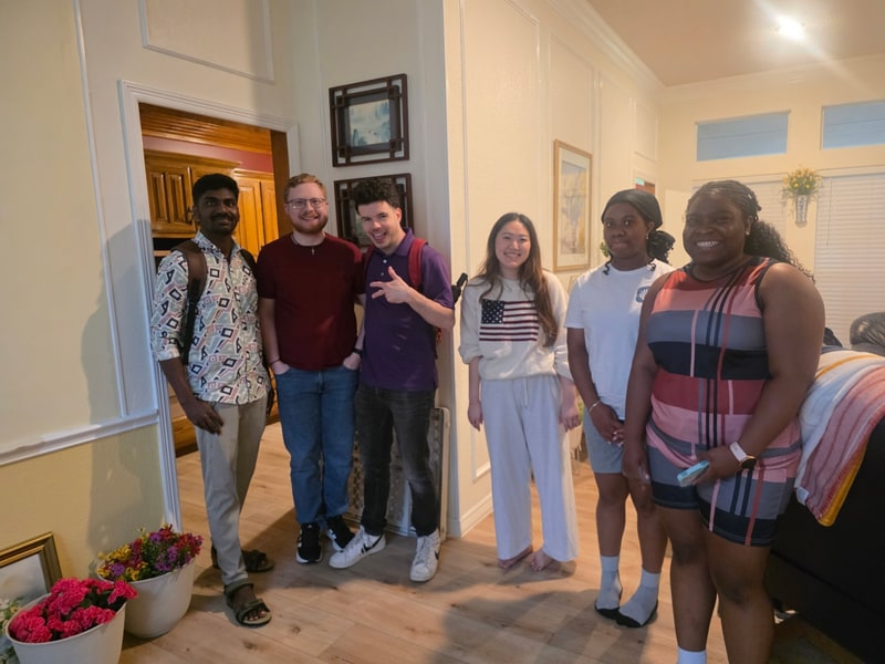 Six friends standing together in the entryway of a home.
