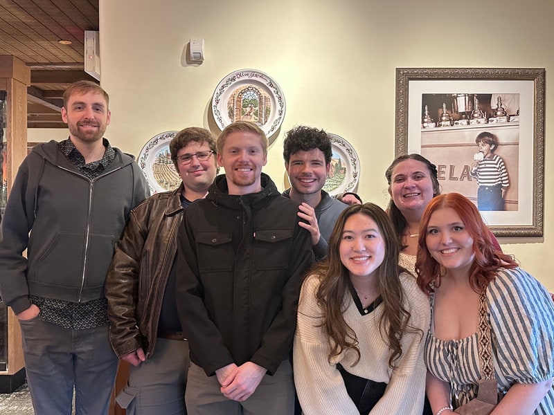 Seven friends smiling together at a restaurant.
