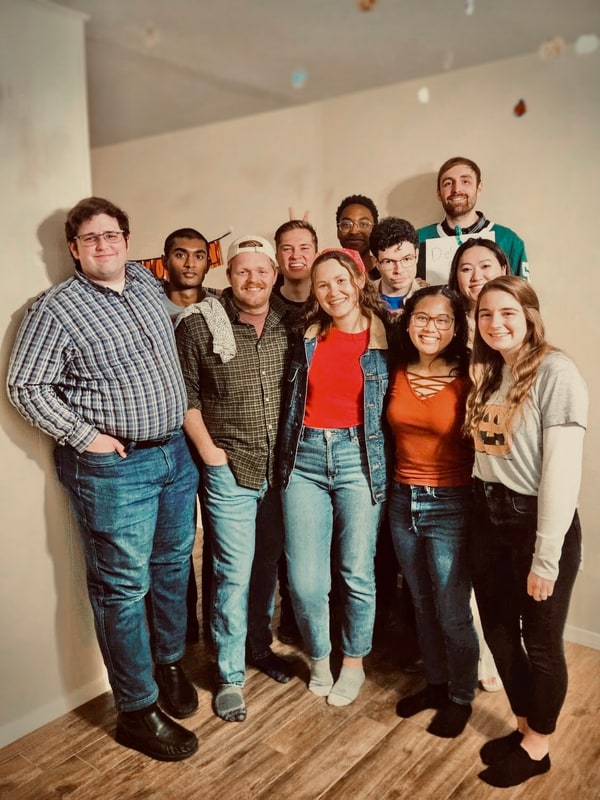 A dozen friends posing together at a fall get-together, one in a pumpkin T-shirt.