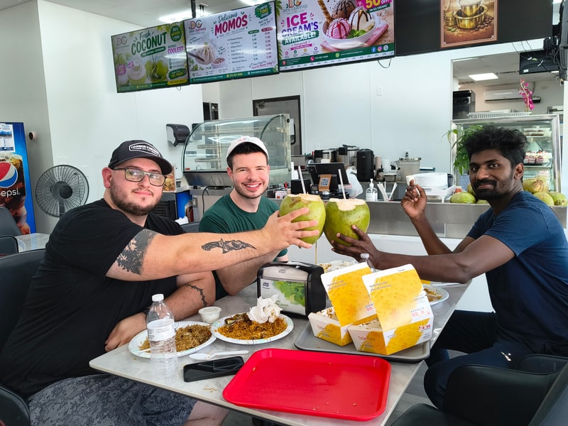 Three friends at a restaurant table raising fresh coconuts in a toast over lunch.